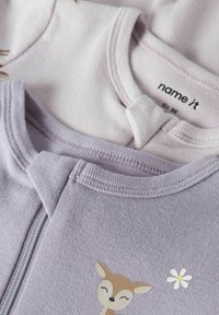 Deux vêtements en coton violet clair avec un col rond. L'un présente un motif de cerf et une fleur, l'autre est uni sans design.