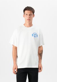 White short-sleeve t-shirt made of cotton. Features blue graphic design on the chest with a patterned headphone motif and adidas logo.