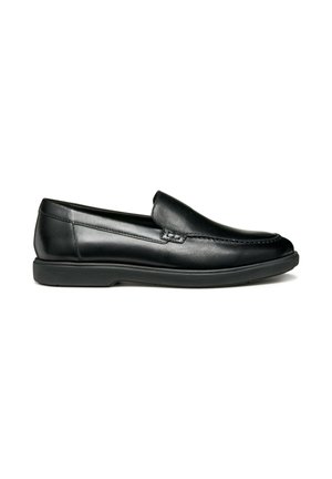 Mocasín de cuero negro sin cordones con detalle de costura, tacón bajo y suela de goma, mostrado de perfil sobre un fondo blanco.