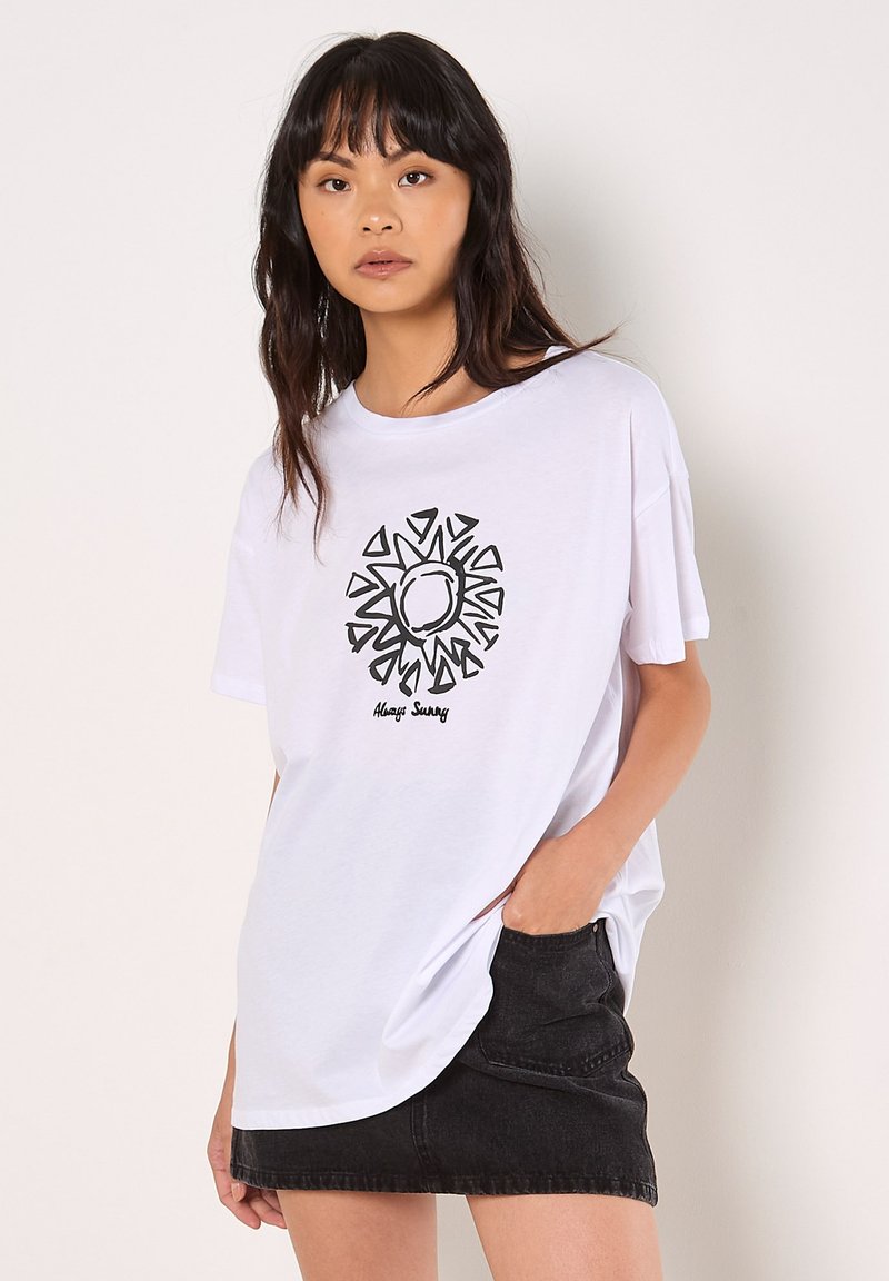 Weißes Baumwoll-T-Shirt mit grafischem schwarzen Sonnenmotiv und dem Text "Always Sunny". Lässiger Schnitt, kurze Ärmel, getragen mit einem schwarzen Jeansrock.