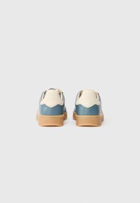 Sneaker in pelle blu e crema con tacco texturizzato, suola in gomma e sistema di allacciatura, caratterizzati da accenti a contrasto e una finitura liscia.