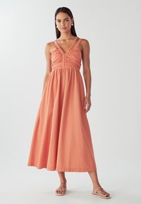 Korallikarva maksikleit kortsuga bodiis, kitsaste rihmade ja voolava seelikuga. Pehme kangas ja lihtne disain, mida on kombineeritud minimalistlike sandaalidega.