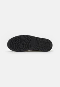 Semelle en caoutchouc noir d'une chaussure Nike avec des motifs de bande de roulement circulaires et en grille visibles sur fond blanc.