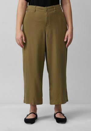 Pantalons larges couleur khaki en tissu doux et texturé. Présente une fermeture à bouton et des passants de ceinture. Portés avec des chaussures plates noires.