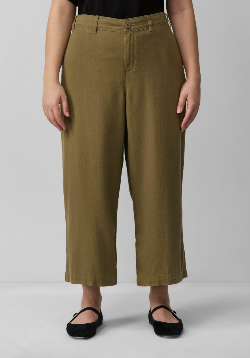 Khaki wijde broek gemaakt van een zachte, gestructureerde stof. Voorzien van een knoopsluiting en riemlussen. Gemaakt in combinatie met zwarte platte schoenen.
