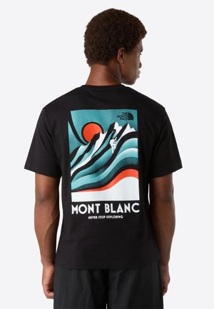Man wearing black T-shirt with a colorful Mont Blanc mountain graphic, climber silhouette, red sun, and "Never Stop Exploring" text on the back.
