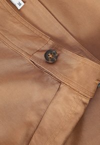 Gros plan sur une ceinture en tissu marron avec un bouton marron et une étiquette de taille "38" sur un vêtement.