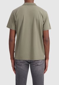 Korte mouwen polo shirt in olijfgroene katoen, met een klassieke kraag en een ontspannen pasvorm, gecombineerd met donkergrijze jeans en subtiele achterzomen.