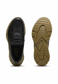 Tenis cu piele neagră și curea, având o talpă din cauciuc bej. Talpa exterioară are caneluri texturate și un logo Puma pe curea.