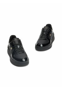 Zapatillas negras con acabado de charol brillante, que cuentan con un collar acolchado, cordones texturizados y una suela texturizada. Acento de logo dorado en el lateral.