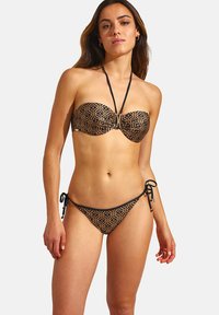 Ensemble de bikini avec un haut bandeau et des bas à nouer sur les côtés. Noir avec un motif géométrique doré. Tissu lisse, matériel minimal, bretelles ajustables.