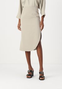 Beige midi skjørt med sidestykke, laget av glatt stoff. Kombinert med svarte høyhælte sandaler med doble spenne-detaljer.