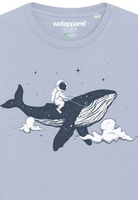 T-shirt bleu clair présentant une illustration sombre d'une baleine et d'un astronaute, entourés d'étoiles et de nuages, dans un design ludique.