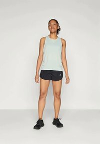 Lyseblå ærmeløs træningstop parret med sorte shorts, der har en afslappet pasform og rund halsudskæring, iført sorte sneakers.