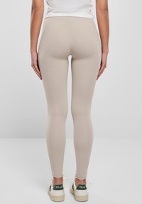 Bež tajice od rastezljivog materijala, uskog kroja, visokog struka, s glatkom teksturom, uparene s bijelim tenisicama koje imaju zelene detalje.