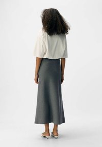 Gray, floor-length skirt made of soft fabric, paired with a loose-fitting white shirt. Features a smooth texture and a clean silhouette.
