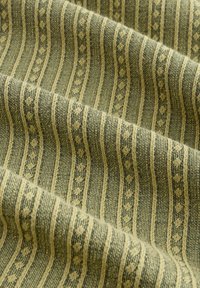 Un tissu à la surface texturée présente des rayures alternées en vert foncé et beige, affichant un motif géométrique et un léger éclat.