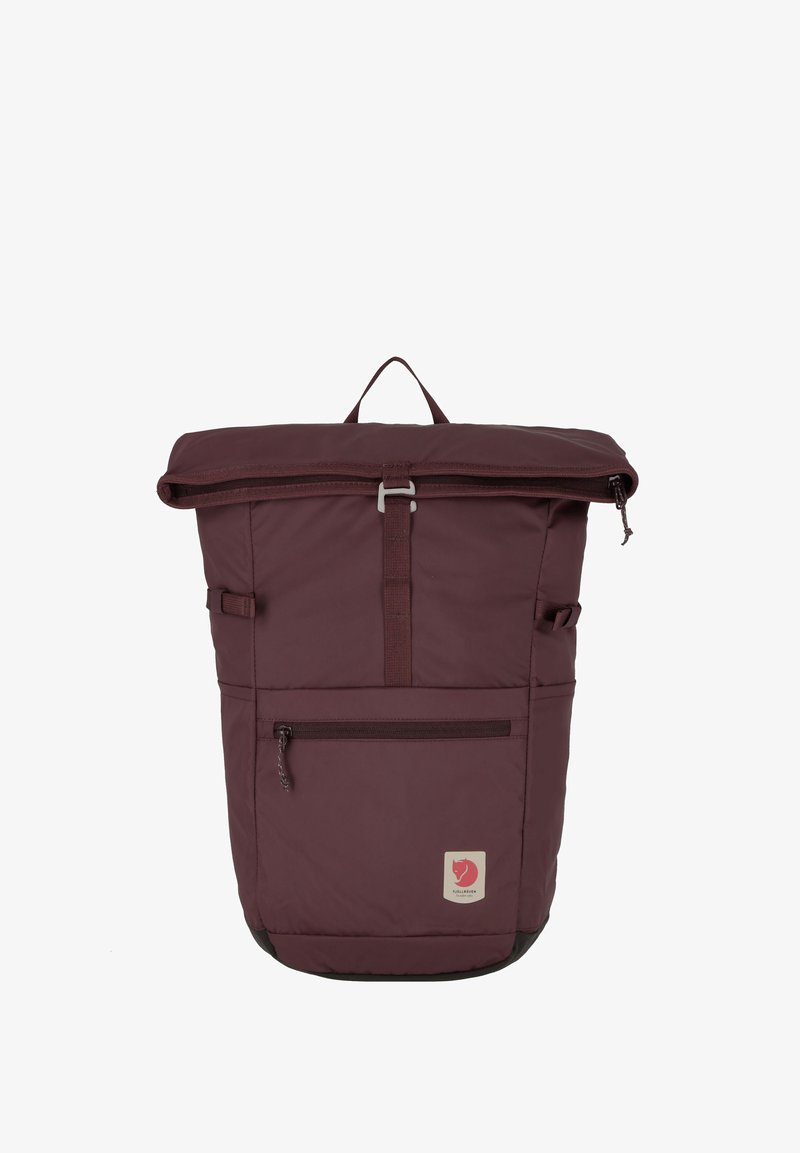 Sac à dos à rabat marron en tissu, avec une poche zippée à l'avant, des bretelles ajustables et une poignée supérieure pour le transport. Comprend un patch logo.