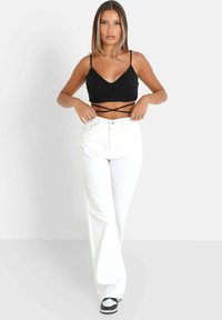 Top cropped nero a coste con spalline incrociate, abbinato a jeans in denim bianchi a vita alta. Sneakers in bianco e nero completano l'outfit.
