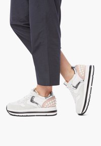 White sneaker with suede and metallic accents, featuring a pink grid pattern at the heel, thick black sole, and lace-up design.