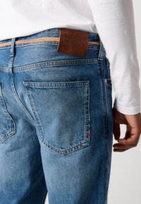 Hellblaue Denim-Jeans mit einem Lederetikett von Scotch & Soda, akzentuiert mit mehrfarbigen Nähten auf den Gesäßtaschen. Klassisches Design, gerade Passform.