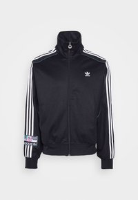 Czarna kurtka z wysokim kołnierzem, białym wzorem trzech pasków na rękawach, zamkiem błyskawicznym z przodu oraz logo na piersi i rękawie.