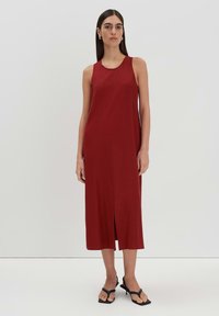 Rotes ärmelloses Midikleid mit Rundhalsausschnitt und einem Schlitz vorne, aus glattem Stoff gefertigt, kombiniert mit schwarzen Riemchenschuhen.