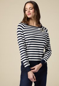 Navy- und weißgestreifter Pullover mit rundem Ausschnitt, gerippten Bündchen und Saum; verfügt über eine dekorative Brosche an der linken Schulter.