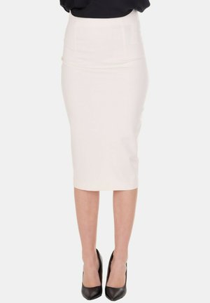 Donna che indossa una gonna a matita color crema, a vita alta e lunghezza fino al ginocchio, abbinata a décolleté nere con punta appuntita e top nero.