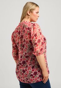 Blusa floreale con maniche a tre quarti in tessuto rosa trasparente, decorata con fiori rossi e viola e dal taglio morbido. Dettaglio dei polsini elasticizzati.