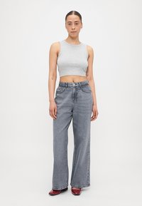 Grå, kort tank topp kombinert med høyt liv og vide grå jeans. Glatt tekstur, subtil falming og kontraststing. Røde sko.