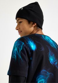 Sort beanie og T-shirt med kort ærme i et blåt flamme-mønster på sort baggrund, der viser en afslappet pasform og et livligt design.