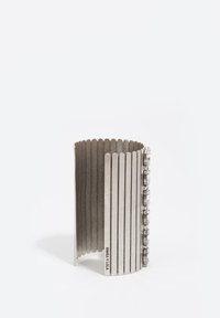 Brazalete de metal con borde festoneado y tiras verticales de metal, con piedras preciosas transparentes decorativas a lo largo de un lado. Color plateado.