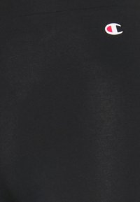 Czarna bawełniana tkanina o gładkiej fakturze. Małe logo w białym i czerwonym kolorze w lewym dolnym rogu. Minimalistyczny design, brak wzorów.