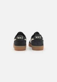 Chaussures Nike en cuir suédé noir et cuir, avec des semelles plates, présentant un logo blanc sur des onglets de talon noirs et une semelle en gomme.