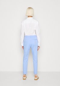 Bílé dlouhé rukávy tričko a světle modré kalhoty s elegantním designem a hladkou texturou. Hnědé detaily na botách, volný střih.