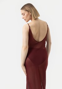 Abito borgogna con schiena bassa e spalline sottili, caratterizzato da una texture trasparente. Il design è aderente e scivola delicatamente all'orlo.