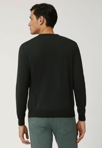 Maglione nero a maglia con maniche lunghe e scollatura rotonda, caratterizzato da una superficie liscia e polsi a coste, abbinato a pantaloni verde chiaro.