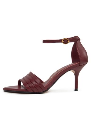 Sandalia de tacón alto color burdeos con diseño de punta abierta, con pliegues horizontales en la parte frontal, una pulsera en el tobillo y un accesorio de hebilla dorada.