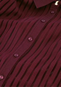 Bordeaux knoopshirt met verticale gestructureerde strepen, voorzien van vier ronde knopen en een kraag. Het materiaal lijkt glad en geweven.