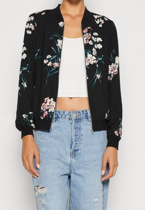 Giubbotto bomber nero con stampa floreale, polsini e orlo a costine, chiusura con zip e vestibilità comoda. Abbinato a jeans chiari strappati.