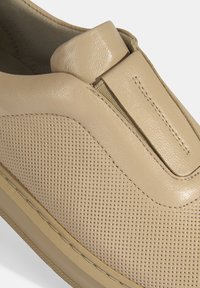 Beige instapschoen met geperforeerd leren bovenwerk, platte rubberen zool en gestikte accenten voor extra detail. Gladde textuur overal.