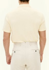 Ljusgul kortärmad polo skjorta, i kombination med beige strukturerade byxor med bakfickor och knappar.