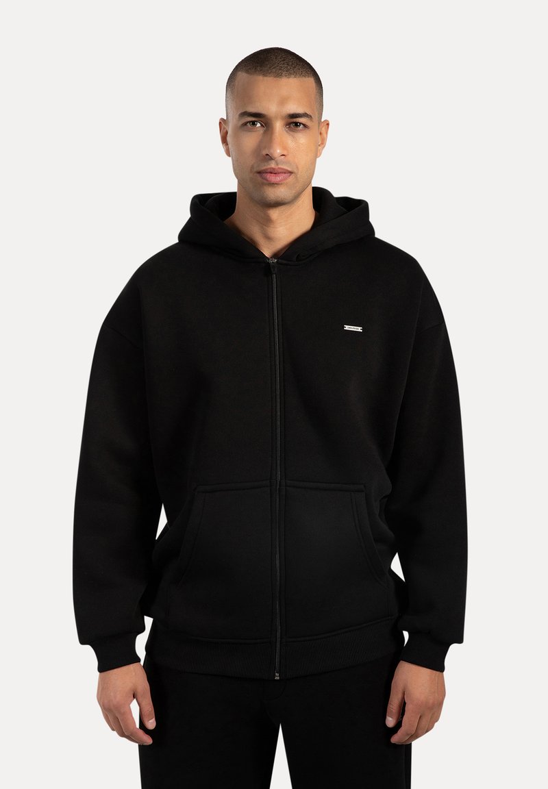 Sort zip-hoodie lavet af blød stof, med en frontlomme, ribbede ærmer og kant, samt et lille logo på brystet.