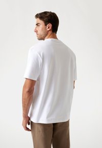 Hvid bomulds t-shirt med korte ærmer, rund halsudskæring og en afslappet pasform, parret med beige bukser. Glat tekstur, ingen synlige mønstre.