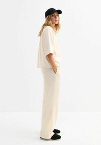 Beige oversized t-shirt en wijdvallende broeken, beide van zachte stof. Een zwarte pet en zwarte schoenen maken de outfit af. Minimalistisch ontwerp.