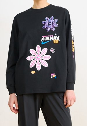 Personne portant une chemise à manches longues noire avec des graphiques floraux colorés Nike Air Max et le texte "Doing it the Air Max way" et "Just do it" à l'avant.