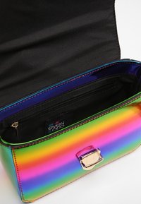 Holografische rechteckige Tasche mit glänzendem Finish, versehen mit einem goldenen Verschluss und einem schwarzen Stoffinnenfutter mit Reißverschlusstasche.