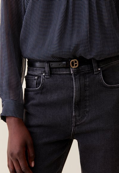 Jeans de mezclilla negros con un ajuste Slim y lavado oscuro. Combinados con una camisa de seda azul marino con un patrón de lunares blancos. Cinturón de cuero negro.