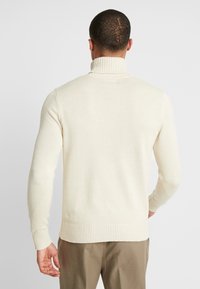 Pull en tricot de couleur crème avec col haut côtelé, manches longues et ourlet côtelé. Présente une texture lisse et une silhouette ajustée.
